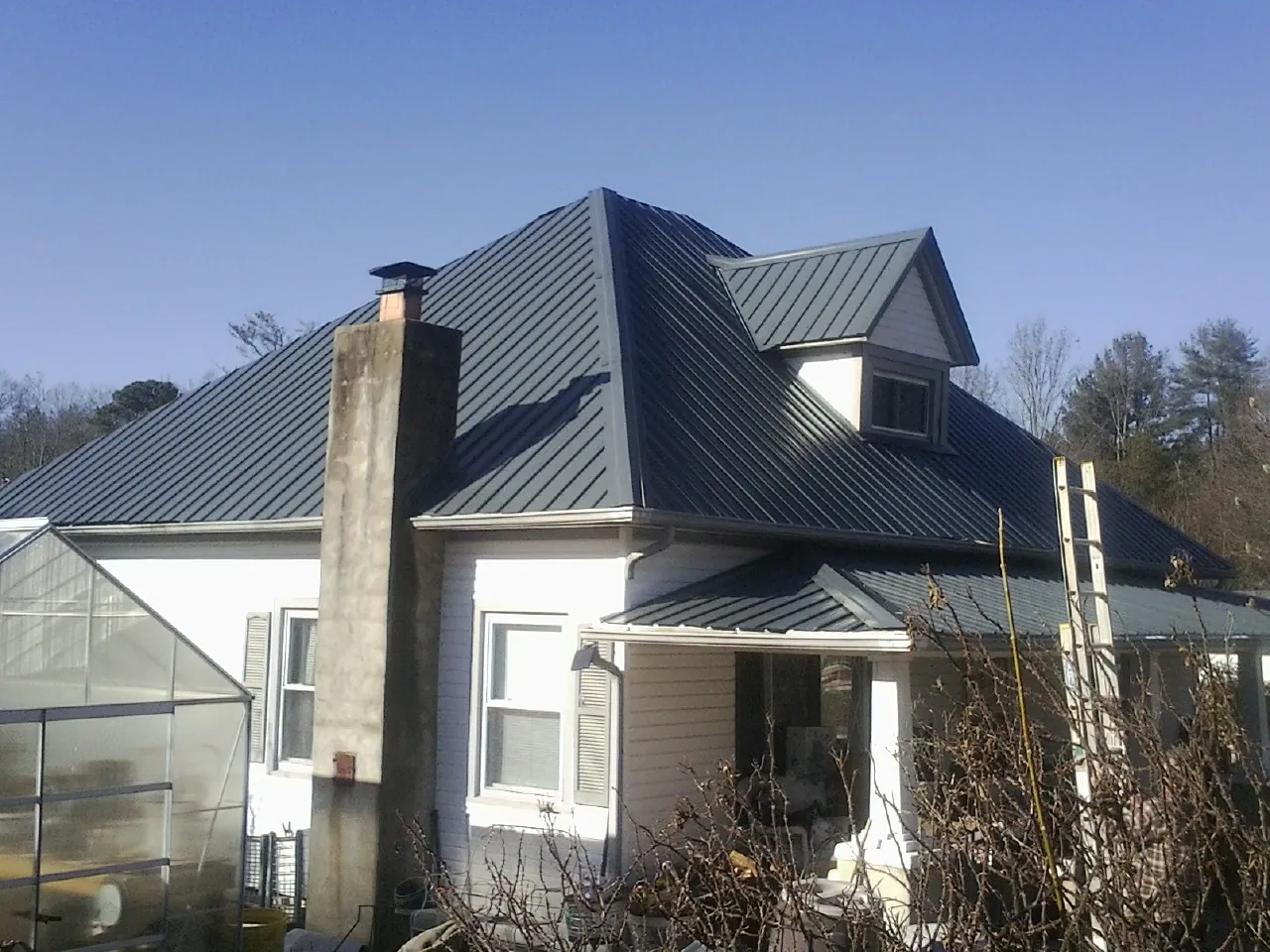 Dark blue standing seam metal roof on a white farmhouse with dormer — Slate & Tile Roof Repair by Roofing Brothers in Ossian