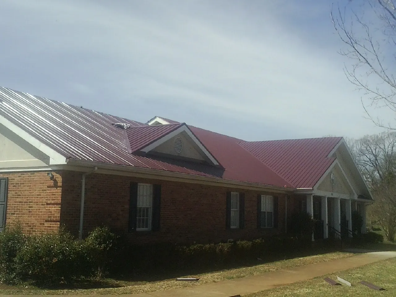 Red metal roof with gabled entries on a long brick building, from a Hail Damage Roof Repair job in Ossian