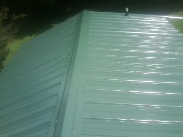New green metal panels meeting at the ridge of a roof — Flat Roof Repair work by our crew in Ossian