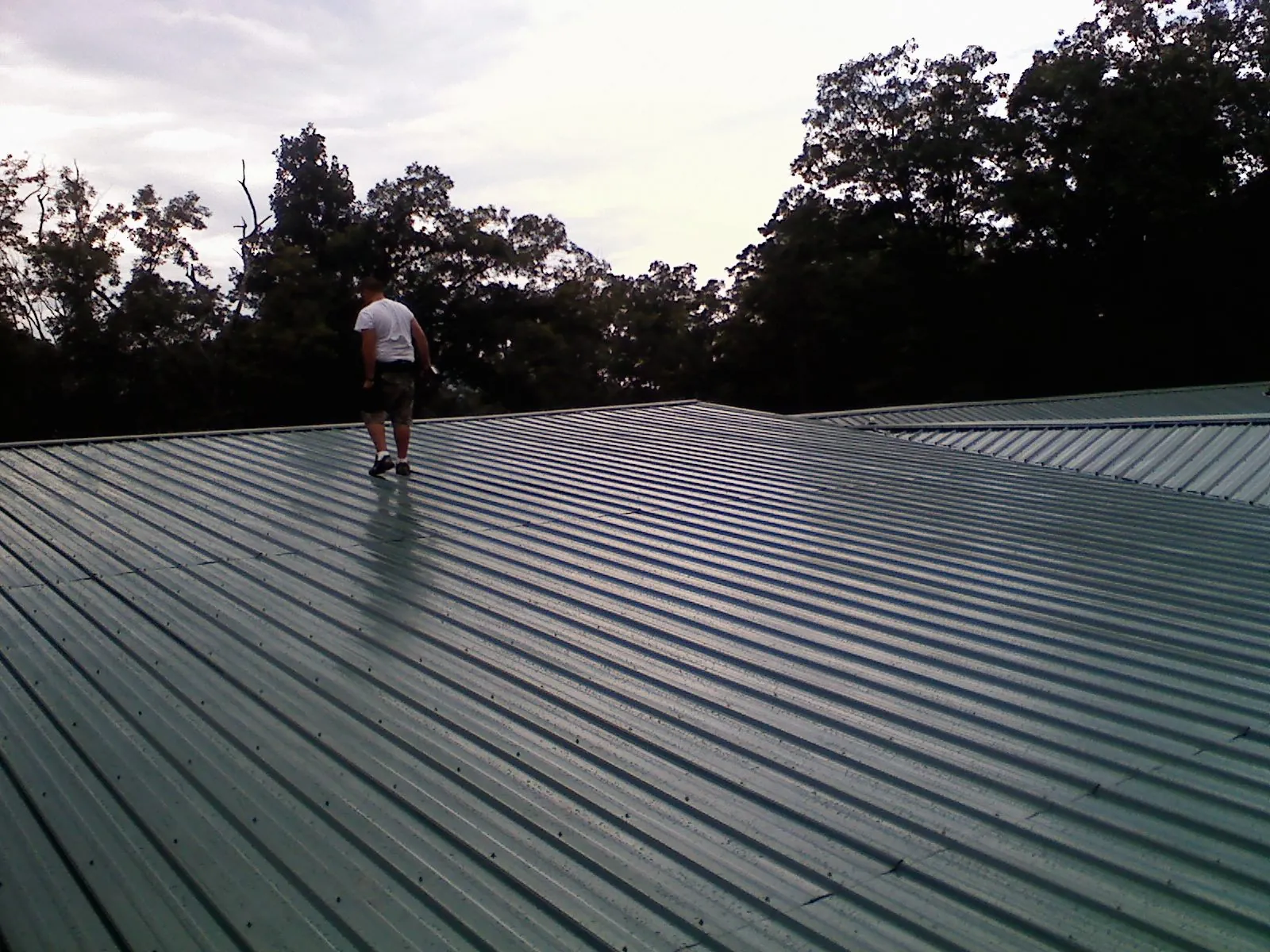 Roofer walking a wide expanse of new green metal roofing in Ossian