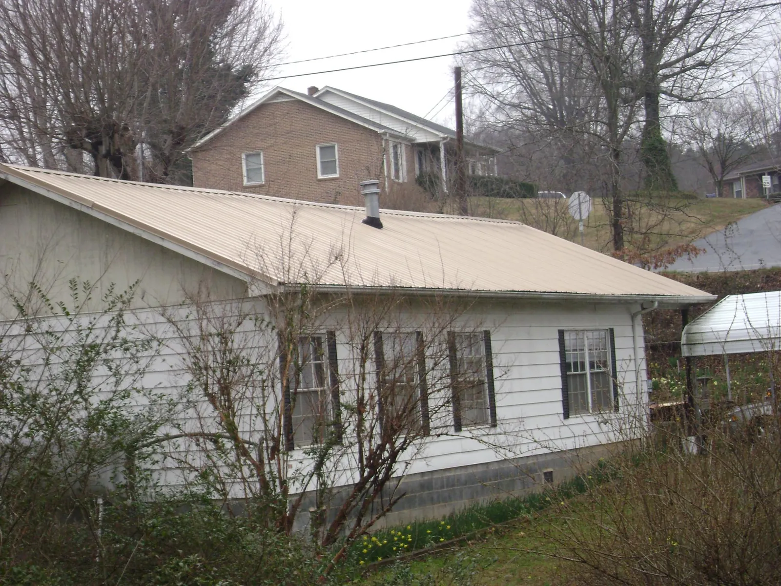 Tan metal roof on a white sided house set into a hillside — Commercial Roofing by Roofing Brothers in Ossian